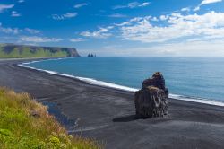 Rocce a Cape Dyrholaey, il punto più a sud dell'Islanda. La sabbia nera della spiaggia contrasta l'azzurro del mare  e il verde splendente della vegetazione.

