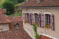 Saint-Cirq-Lapopie (Francia): una graziosa casa in pietra con fiori alle finestre e persiane in legno, Occitania.
