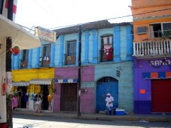 San Pedro Pochutla: sulla strada principale che attraversa la cittadina si affacciano case dai colori accesi che contribuiscono a rendere, se possibile, ancora più caotico e vivace il ...