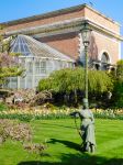 La scultura in bronzo di una donna seduta su una sedia: si trova nel giardino botanico di Leuven, Belgio. Sullo sfondo, un prato fiorito - © Tina Vander Molen / Shutterstock.com