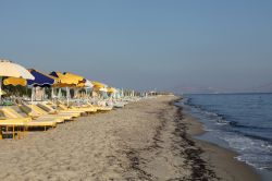 Lettini e ombrelloni sulla spiaggia di Tigaki a Kos, Grecia. Grazie ad una leggera brezza marina, questa località è perfetta per praticare surf, sci d'acqua e vela - © ...
