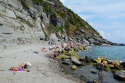 Turisti sulla spiaggia rocciosa di Vernazza, La Spezia, Liguria.  Il paese è incastonato in una baia fra i Comuni di Monterosso al Mare e Riomaggiore - © JanHetman / Shutterstock.com ...