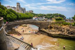 La splendida veduta di una spiaggetta cittadina a Biarritz con ponte e scalinata, Francia. Sullo sfondo, la chiesa di Santa Eugenia, costruita nel 1898 nel luogo in cui si trovava la cappella ...