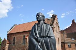 La statua di Heuric Schartou a Lund (Svezia) con l'edificio religioso del Liberiet sullo sfondo.
