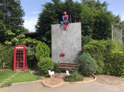 Statua di Spiderman seduto su un muro nella città di Suphan Buri, Thailandia. Sotto, una panchina con due agnellini e una cabina telefonica rossa - © I Love Coffee dot Today / Shutterstock.com ...