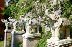 Statue di elefanti allo Scherrer Park di Morcote, Svizzera. Sul muro ricoperto di vegetazione sono incastonate raffigurazioni di serpenti e di mucche - © Stefano Ember / Shutterstock.com ...