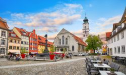 Tavolini di un ristorante all'aperto nella piazza di Lindau, Germania. Sullo sfondo, la chiesa e le tipiche case bavaresi.

