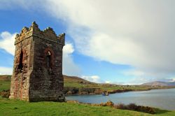 Vecchia torre in pietra a Dingle, Irlanda. Questa antica costruzione in pietra si affaccia sulla baia di Dingle. Sullo sfondo, una barca con le reti gettate in mare - © Sean O' Dwyer ...