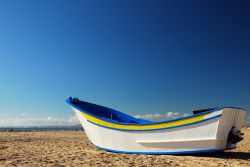 Una tradizionale barca da pesca sulla spiaggia vuota di Costa da Caparica, Portogallo.


