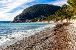 Un tratto di spiaggia di Eze-sur-Mer (Francia) con le montagne ricoperte di vegetazione sullo sfondo.

