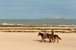 Trekking a cavallo sulla spiaggia nei pressi di Seahouses, Inghilterra. In lontananza sull'isola di Inner Farne il faro bianco - © Vincent MacNamara / Shutterstock.com 
