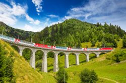 Il treno Glacier Express mentre attraversa il famoso ponte sul viadotto Landwasser in estate (Svizzera). Questo spettacolare ponte in pietra a sei archi varca la profonda gola in cui scorre ...