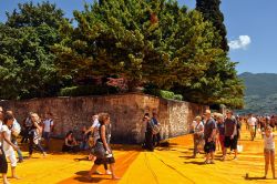 Turisti a Peschiera Maraglio fotografati mentre camminano sulle Floating Piers di Christo, nel tratto in cui costeggiano il Monte Isola sul Lago di Iseo - © s74 / Shutterstock.com ...