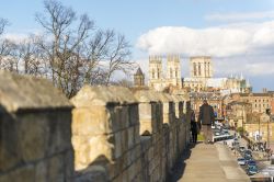 Turisti a piedi lungo le mura medievali che circondano il centro storico della città di York, in Inghilterra. Sullo sfondo si può distuinguere The Minster, la cattedrale di York - ...