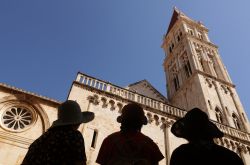 Turisti ammirano la chiesa di San Sebastiano in piazza Giovanni Paolo II° a Trogir, Croazia. Costruito nel 1476, questo edificio non viene più utilizzato per cerimonie religiose: ...