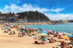 Turisti in relax sulla spiaggia di Blanes, Costa Brava, Spagna. Lungo la costa di questa località si alternano scogliere e insenature tranquille - © S-F / Shutterstock.com