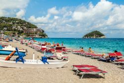 Turisti in spiaggia a Spotorno, provincia di Savona, con ombrelloni e sdraio. Sullo sfondo, l'isola di Gallinara - © Olgysha / Shutterstock.com