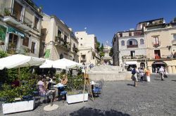 Turisti seduti nel dehors di un bar in Piazza del Duomo a Taormina, Sicilia. Raccolta e suggestiva, questa piazza di Taormina ospita al suo centro una fontana barocca in pietra dove si trova ...