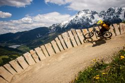 Un biker percorre il Wall Ride in legno in un parco-bici a Leogang, Austria. Sullo sfondo, vette alpine innevate - © Victor Lucas Photography / Shutterstock.com