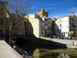 Un canale della città di Narbonne, Francia. Sullo sfondo, un ristorante con tavolini all'aperto.
