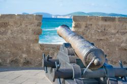 Un cannone sui bastioni della città di Alghero in Sardegna. Sullo sfondo la costa di Capo Caccia - © Gabriele Maltinti / Shutterstock.com