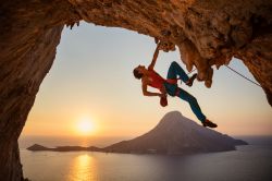 Un climber scala la parete di una grotta sull'isola di Kalymnos, Grecia, al tramonto.



