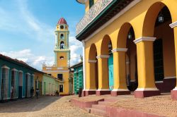 Un edificio coloniale restaurato e, sullo sfondo, la sagoma della chiesa di San Francisco de Asis a Trinidad, Cuba - © gvictoria / Shutterstock.com