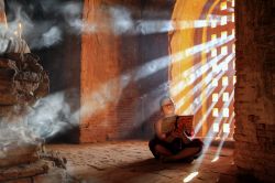 Un giovane monaco intento a leggere all'interno di una pagoda a Bagan, Myanmar. La luce soffusa che entra nella pagoda illumina le pagine del libro che questo giovane religioso buddista ...
