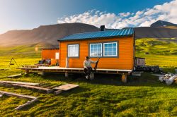 Un paesaggio naturale delle montagne di Spitsbergen a Longyearbyen, isole Svalbard, Norvegia. Un cacciatore, seduto davanti a una casetta in legno, osserva il tramonto dell'estate artica.
 ...