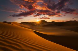 Un suggestivo tramonto dai colori infuocati nell'oasi di Douz, Tunisia. Osservare il cielo stellato o il tramonto e l'alba fra le dune del deserto è una delle esperienze più ...