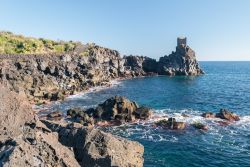 Un tratto di costa rocciosa della scogliera vicino a Acireale, Sicilia. Sullo sfondo, una torre di guardia.

