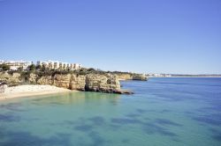 Un tratto di litorale a Armacao de Pera, Portogallo. Lasabbia dorata è lambita dall'acqua di un mare azzurro e sereno che si estende a perdita d'occhio.
