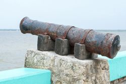Un vecchio cannone arrugginito su un blocco di cemento lungo la baia di Chetumal, Messico. Sullo sfondo, la costa del Belize.

