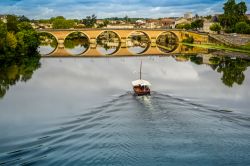 Una barca solca il fiume Dordogna a Bergerac, Francia. Sullo sfondo, il vecchio ponte che si riflette sull'acqua.
