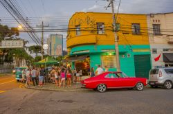 Una bella automobile rossa parcheggiata all'angolo di una strada a Curitiba, Brasile. Fuori da un ristorante la gente attende il proprio turno - © Fotos593 / Shutterstock.com