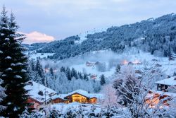 Una bella veduta invernale della vallata di Les Gets, Francia, di sera. A illuminarla, le luci di baite e case in legno.



