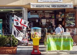 Una bottega di tipici prodotti gastronomici e souvenir a Olbia, Sardegna. In primo piano, su un lato, la bandiera dei quattro mori sventola al vento  - © Cebas / Shutterstock.com