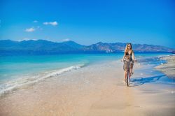 Una donna in bicicletta si rilassa sull'isola tropicale di Gili Air, Indonesia. Quest'isolotto è circondato da un candido litorale sabbioso e da acque trasparenti popolate da ...