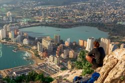 Una donna seduta su una collina del Penon de Ifach ammira la città di Calpe, Spagna.

