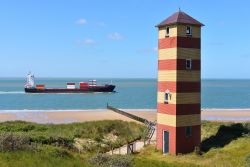 Una nave cargo nelle acque davanti alla costa di Vlissingen, Olanda. In primo piano, un faro a strisce. 

