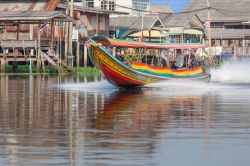 Una piroga colorata sul fiume Chao Phraya a Nonthaburi, Thailandia. Sullo sfondo, le tradizionali case thai - © Nbeaw / Shutterstock.com