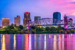 Una pittoresca skyline della città di Little Rock lungo il fiume Arkansas (USA): al crepuscolo le luci di palazzi e strutture si riflettono nell'acqua.

