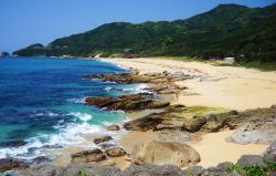 Una spiaggia di sabbia bianca sull'isola di Yakushima, Giappone. Sullo sfondo, montagne con vegetazione rigogliosa.

