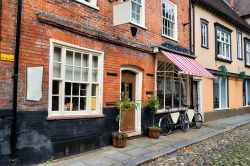 Una strada ciottolata con negozi nel centro del villaggio di Norwich, Norfolk, Inghilterra.

