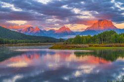 Una suggestiva alba al Grand Teton National Park in Wyoming, USA. I riflessi rossastri del cielo si riflettono nell'acqua del fiume Snake, il più lungo del parco.

