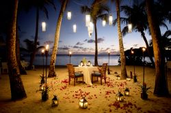 Una tavola apparecchiata in spiaggia sull'isola di Antigua, America Centrale. A rendere più suggestiva l'atmosfera già romantica sono la luce delle lanterne e i petali ...