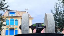 Una vecchia macina di fronte a un edificio dalle finestre azzurre e blu a Celle Ligure, Liguria.
