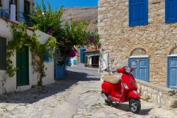 Una viuzza dell'isola di Chalki, Grecia, con una vespa color rosso parcheggiata.



