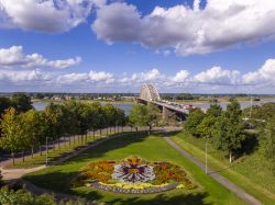 Uno scorcio del ponte sul fiume Waal nella città di Nijmegen, Olanda. In primo piano lo stemma della città fatto con i fiori in un parco.
