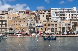 Uno scorcio della città di Marsascala, isola di Malta, con edifici sullo sfondo. In primo piano, l'acqua del Mediterraneo con barche da pesca - © Yassmin Photo / Shutterstock.com ...